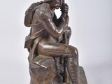 bronze statue of a man sitting on a rock with his hand on his chin