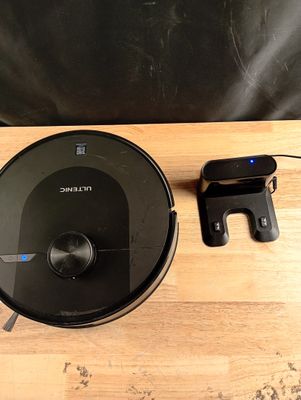 a black robot sitting on a wooden table next to a cell phone
