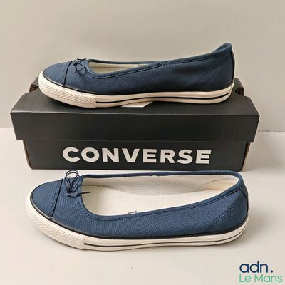 des Converse sans lacets, bleues avec des semelles blanches, posées sur une boîte