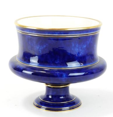un vase bleu bordé d'or posé sur une surface blanche