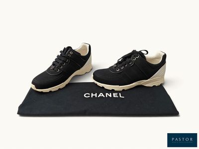 baskets Chanel noires à semelles blanches posées sur un tapis noir