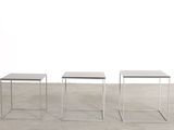 three white tables sitting on top of a cement floor next to a white wall