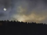 smoke billows from a forest fire as the sun sets in the distance