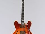 une guitare électrique orange suspendue à une ficelle sur un mur blanc