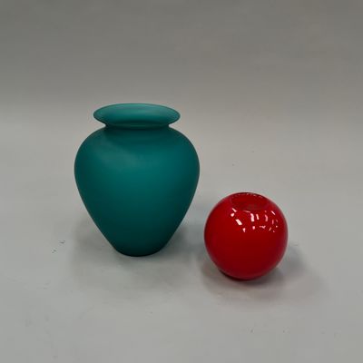 un vase bleu à côté d'une balle rouge posée sur une surface blanche