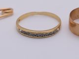 two gold wedding rings and a pin on a white surface