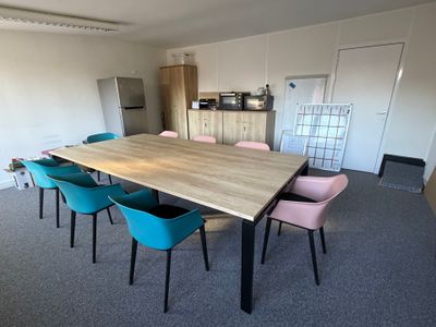 Des chaises aux couleurs vives sont disposées autour d'une table en bois dans une pièce vide.