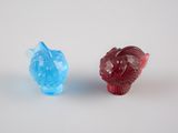 deux figurines en verre de couleurs différentes posées sur une surface blanche