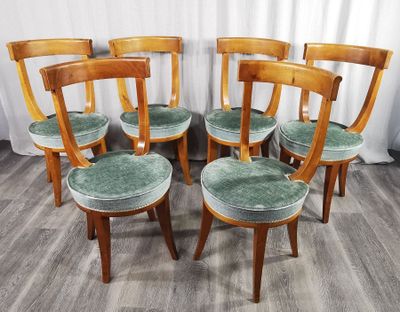 six chaises en bois avec des assises rembourrées vertes, devant un rideau blanc