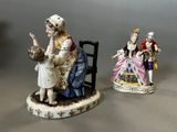 two figurines of people sitting on a chair and one holding a cat