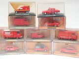 Six petites voitures rouges sont exposées dans une vitrine posée sur une surface blanche.