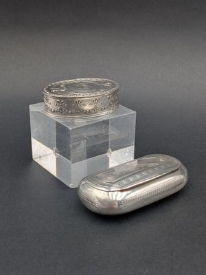 un récipient en verre muni d'un couvercle en argent, à côté d'un comprimé argenté