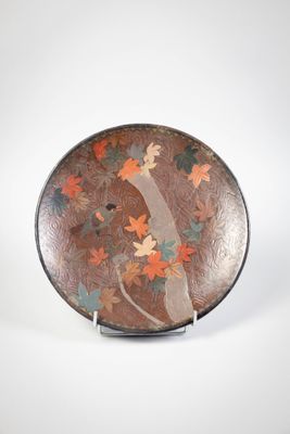 brown plate with orange and green leaves on it sitting on a stand
