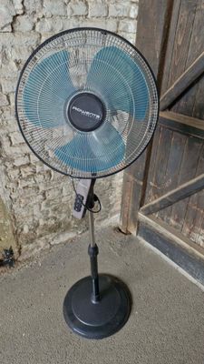 a fan that is sitting on a stand in front of a brick wall