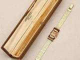 an image of a watch in a wooden box with a gold band