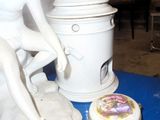 a statue of a boy sitting on a table next to a pot and a cup