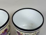 two cups with flowers painted on them on a white surface