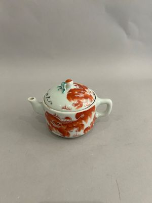 a small white and red pot with a lid on a table