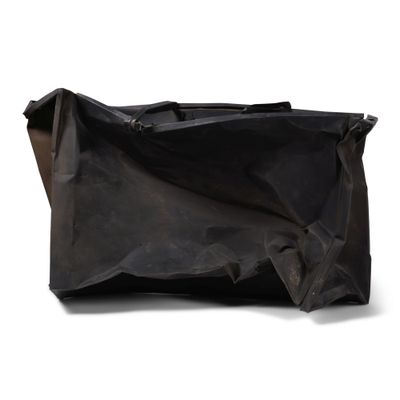 Le grand sac noir est posé par terre, près d'un mur blanc.
