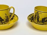 pair of yellow and black cups and saucers with figures on them