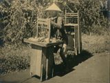 a black and white photo of a man sitting at a table with a bird cage on it