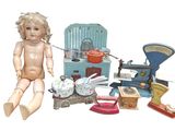 une poupée assise par terre à côté d'un tas de vieux jouets