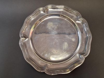 an antique silver plate with a scalloped edge on a black surface