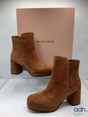 une paire de bottines en daim marron, avec une boîte en arrière-plan