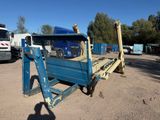 un camion à plateau bleu garé sur un parking, avec d'autres camions en arrière-plan