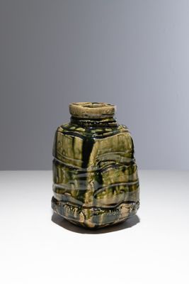 un vase vert posé sur une table, sur fond gris