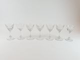 six clear wine glasses lined up in a row on a white surface