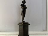 une petite statue en bronze représentant une femme, posée sur un socle