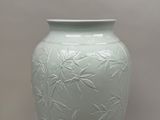 a green vase sitting on a table with a white wall in the background