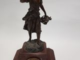 une statue en bronze représentant une femme tenant un panier de fleurs au sommet d'une horloge