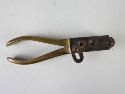 une vieille pince en laiton posée sur une surface blanche