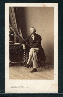 une vieille photo d'un homme en costume, assis sur une chaise