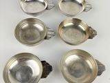 six silverplated dishes with handles and spoons on a white surface