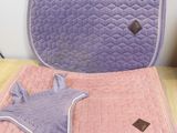 un tapis de selle et une couverture matelassés violets et roses posés sur une table en bois