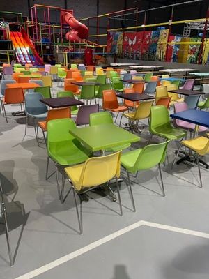 des chaises et des tables aux couleurs vives dans une aire de jeux, avec un toboggan en arrière-plan