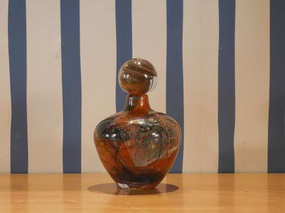 a glass vase sitting on a wooden table with a striped wall behind it