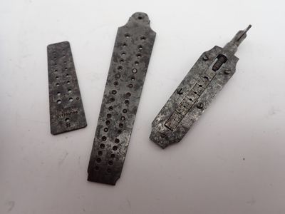 trois morceaux de métal percés de trous, posés sur une surface blanche