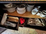 many plates and spoons in the open drawer of a cabinet