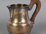 a silver pitcher with a wooden handle sitting on a table