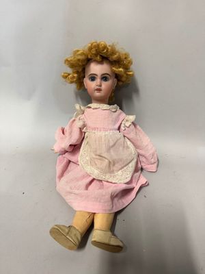 une vieille poupée aux cheveux blonds et vêtue d'une robe rose, assise sur une surface blanche
