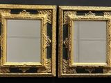 two gold framed mirrors on a black wall in a room