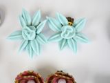 two pairs of pink and blue flower earrings on a white surface