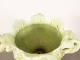 a green vase sitting on a table with a white wall in the background