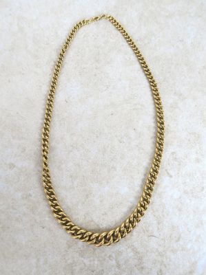 un collier à chaîne en or posé sur une surface en marbre