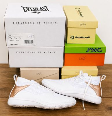 white and gold sneakers on a wooden table next to boxes of boxes