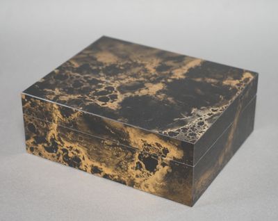 une image représentant une boîte en marbre noir et doré posée sur une surface blanche